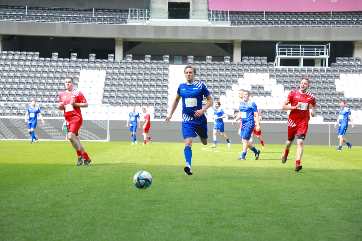 Auf Fußballfeld: Mann in blauen Fußballtrikot läuft Ball nach