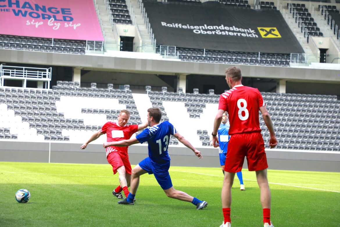 Auf einem Fußballfeld: Mann in rotem Fußballdress, steigt Gegner in blauem Dress auf den Fuß.