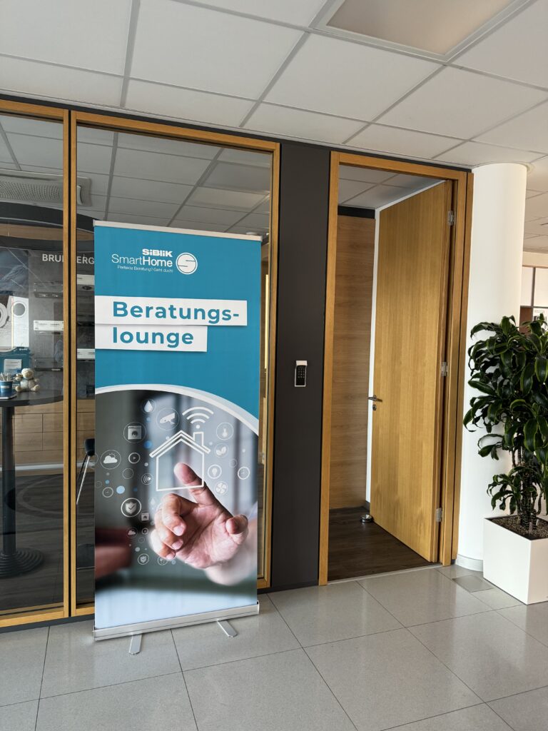 Ein Roll-up-Banner der SIBLIK SmartHome Beratungs-Lounge steht vor einem modernen Büroeingang.