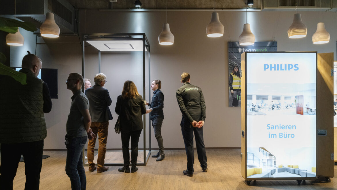 Eine Gruppe von Menschen diskutiert in einem modernen Bürogebäude, umgeben von Signify-Leuchten.