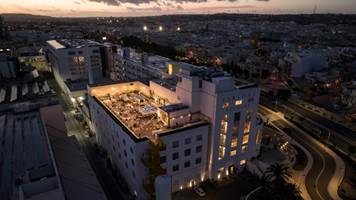 Luftaufnahme eines beleuchteten Stadtgebäudes mit Rooftop-Bereich bei Abenddämmerung.
