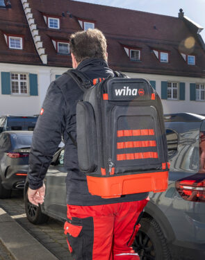 Elektriker trägt den Wiha Werkzeugrucksack auf dem Rücken durch eine Wohnsiedlung.