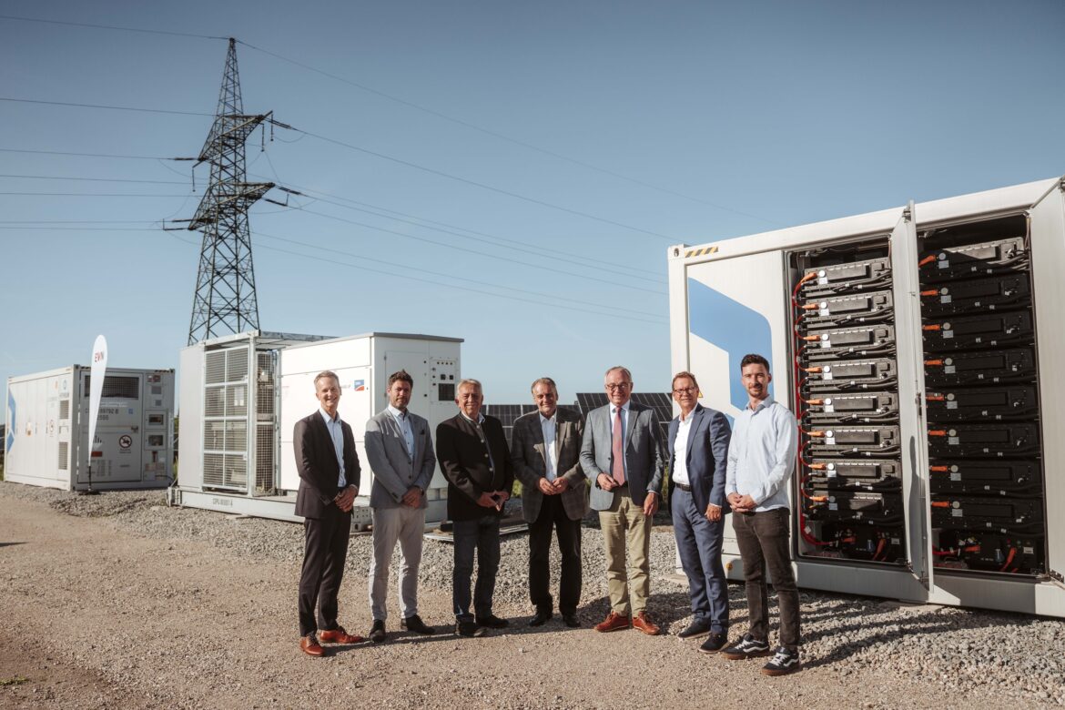 Sieben Männer posieren gemeinsam vor Batteriecontainern und Photovoltaikanlage.