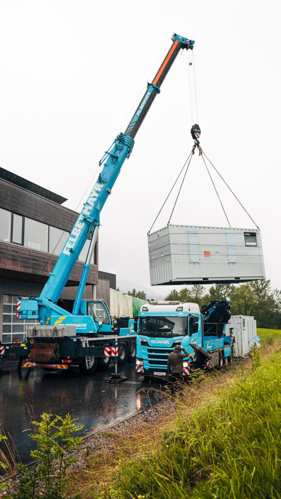 Kran hebt großen Energiespeicher-Container von e.battery systems auf ein Transportfahrzeug.
