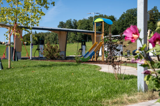 Spielplatz mit Rutsche im grünen Bereich des Ladeparks Amstetten, im Hintergrund Ladeinfrastruktur.