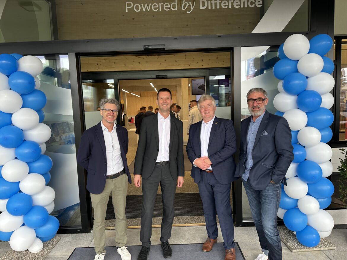 Vier Gäste stehen beim Eingang der neuen Niederlassung unter blau-weißer Ballondekoration.