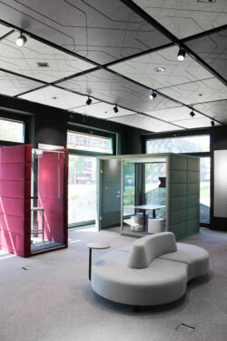 Offener Büroraum mit Akustikdecken, modernen Lichtschienen und farbigen Rückzugsboxen für konzentriertes Arbeiten.