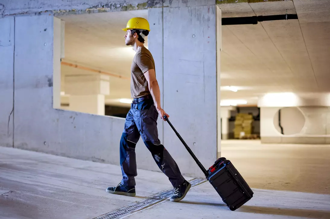 Handwerker zieht den Wiha XL2 Werkzeugkoffer als Trolley mit ausgezogenem Teleskopgriff durch ein Gebäude.