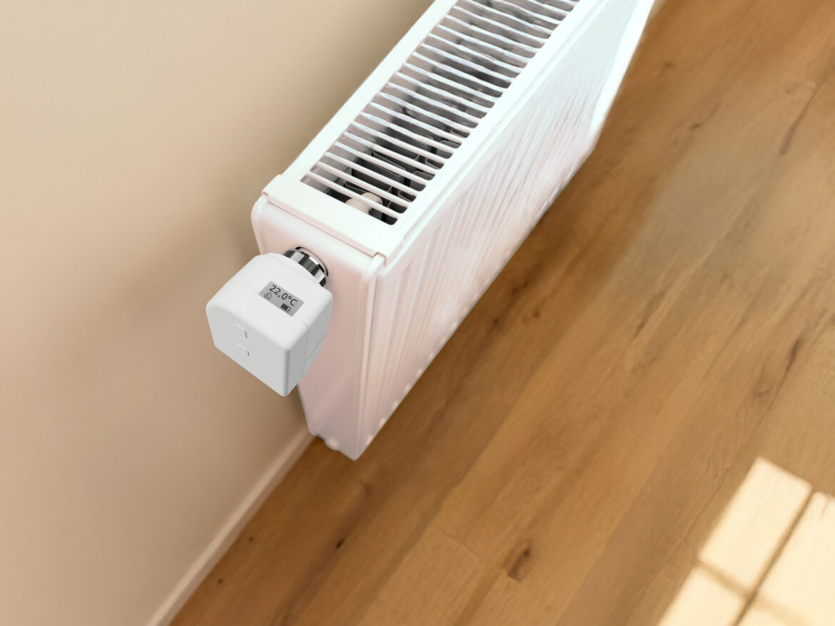 Weißes, digitales Heizkörperthermostat mit Display an einem Heizkörper in einem Wohnraum mit Holzboden.