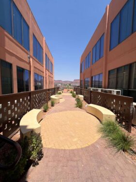 Moderner Innenhof zwischen zwei Gebäuden mit Sitzbänken, Pflanzen und Blick auf Wüstenlandschaft.