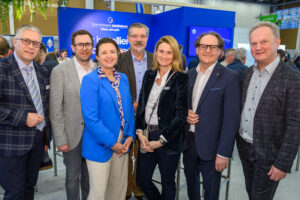 Sieben Personen posieren gemeinsam lächelnd vor dem blauen Messestand der Österreichischen Installateure auf der Messe Wels.