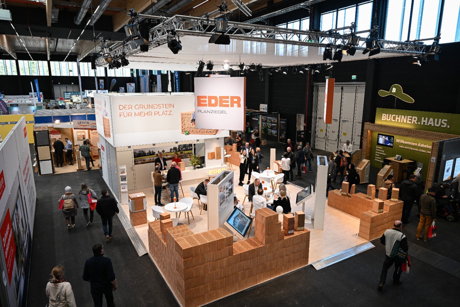 Vogelperspektive auf den Messestand von Eder Planziegel mit gemauerten Ziegelwänden als Raumgestaltung, umgeben von weiteren Ausstellern in einer Messehalle.