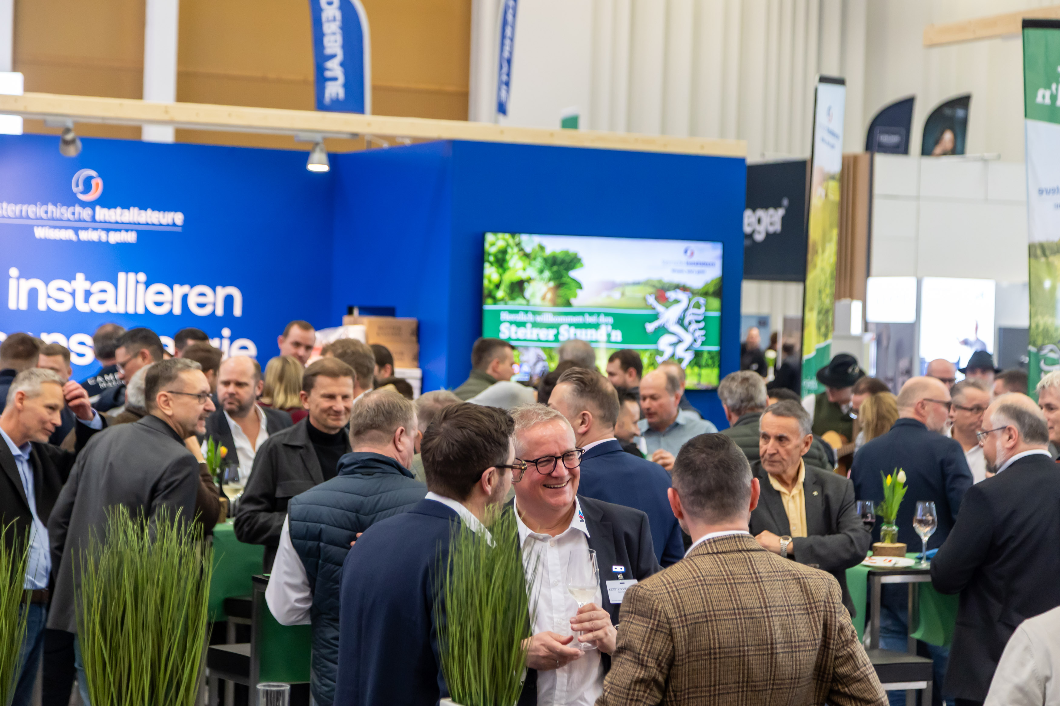 Belebter Netzwerkabend mit zahlreichen Fachbesuchern vor dem blauen Stand der Österreichischen Installateure auf der Messe Wels.