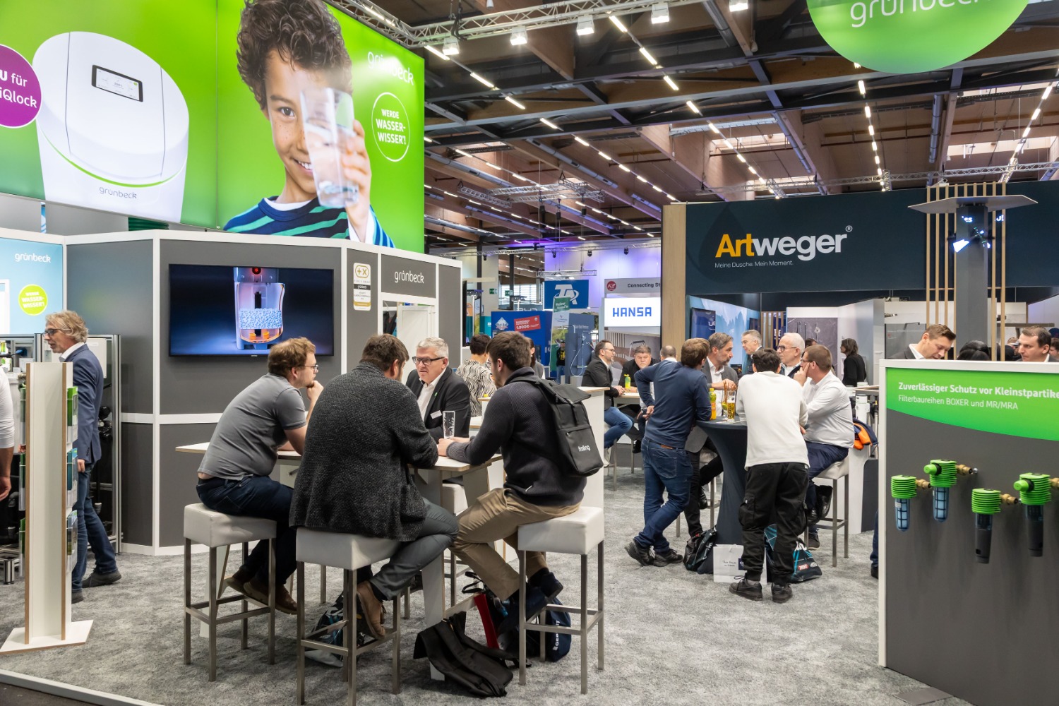 Gut besuchter Messebereich mit den Ständen von Grünbeck und Artweger, an denen Fachbesucher in Gesprächen an Stehtischen sitzen.