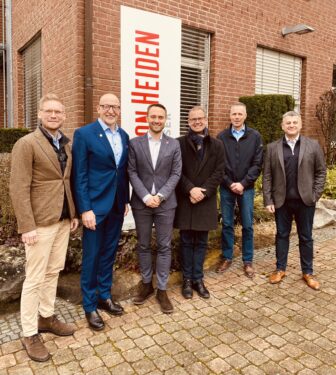 Sechs Männer stehen vor einem Firmengebäude mit Heinz von Heiden Schriftzug. 