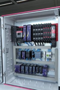 Offener Schaltschrank mit mehreren Puls Netzteilen, Reihenklemmen und verdrahteten Komponenten.