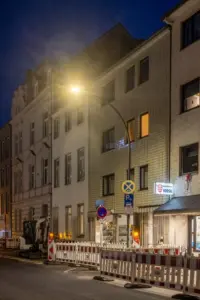 Nächtliche Straßenszene vor der Modernisierung mit Straßenleuchte, Baustellenabsperrungen und mehrstöckigen Gebäuden vor einem Kiosk in Köln.
