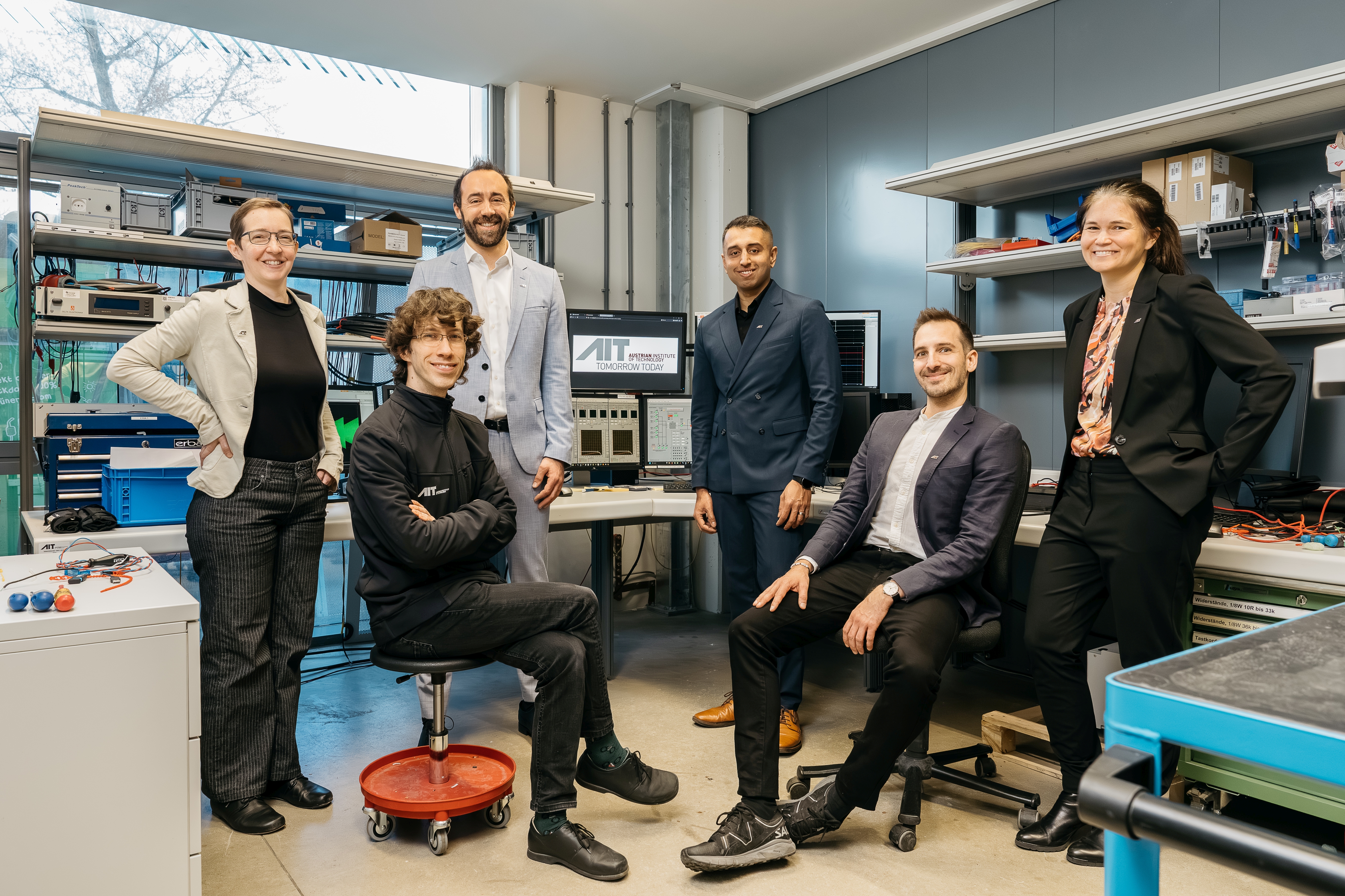 Forschungsteam des AIT steht und sitzt in einem Labor vor technischen Geräten und Computern.