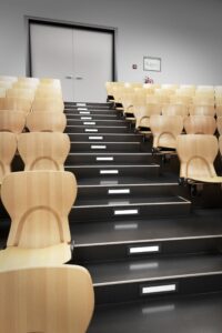 Ansteigender Hörsaal mit hellen Holzsitzen und beleuchteten Stufenmarkierungen zwischen den Sitzreihen.
