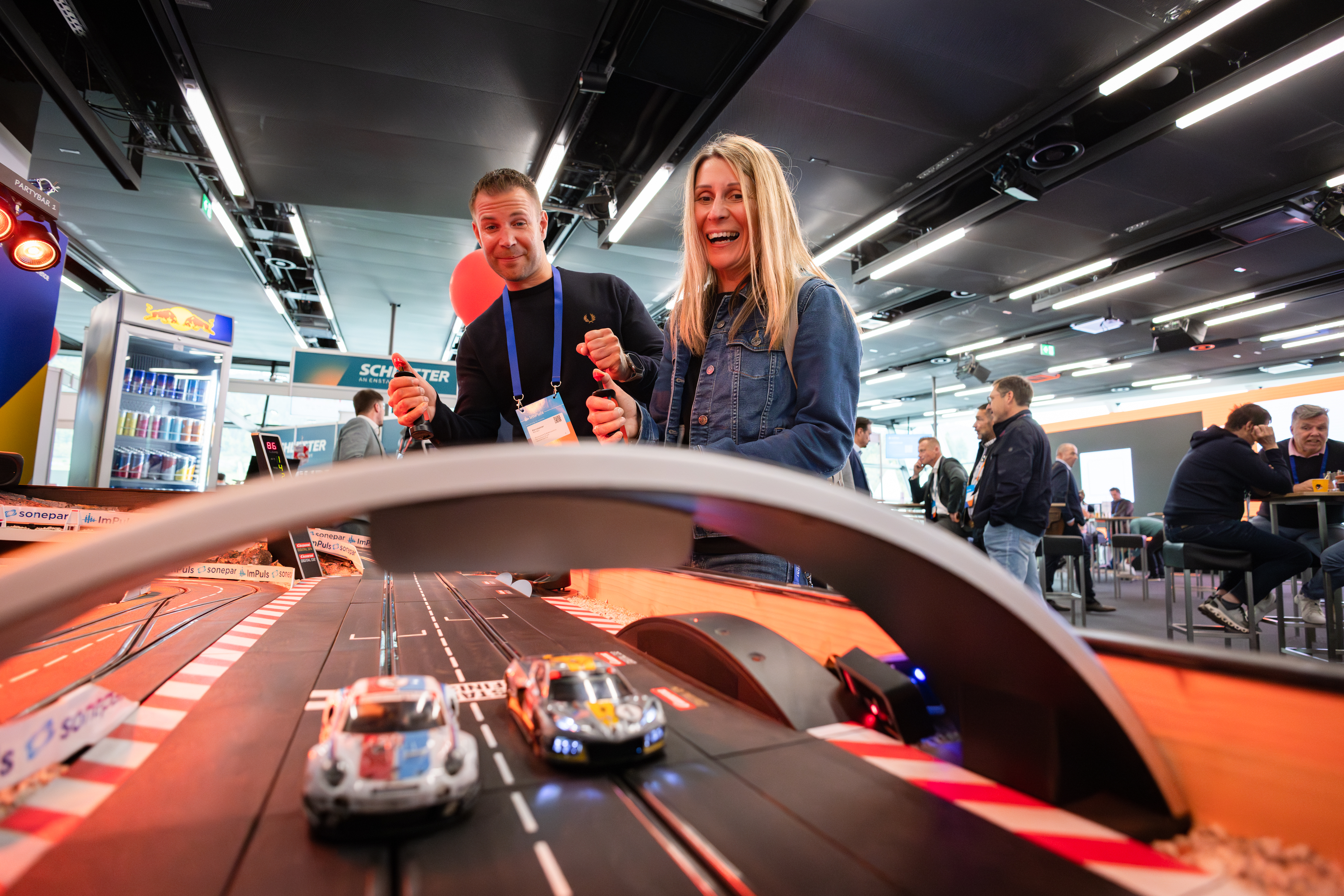 Zwei Personen spielen an einer Carrera-Rennbahn in einer Messehalle.