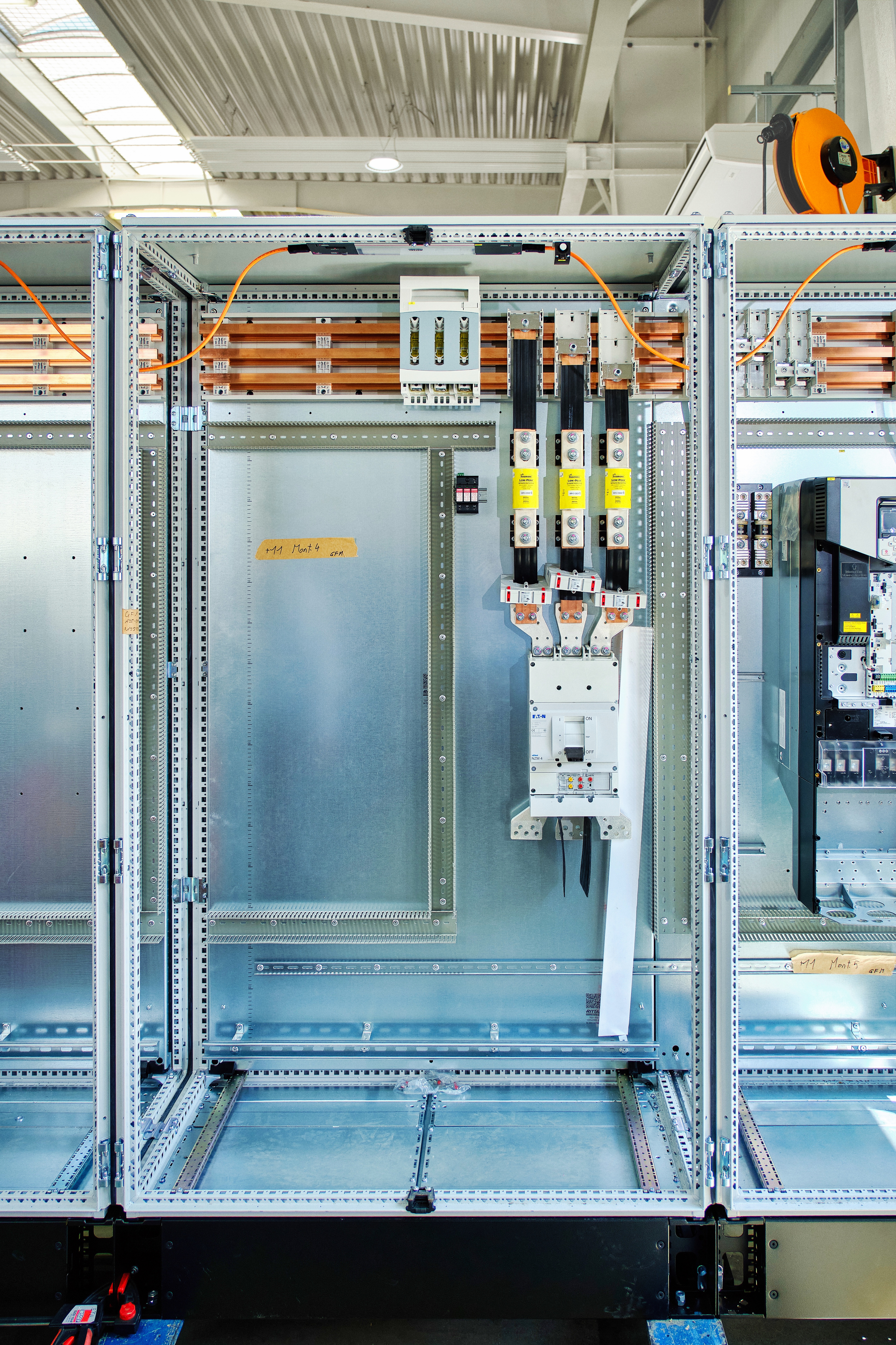 Geöffneter Schaltschrank mit Sammelschienensystem und elektrischen Komponenten in der Fertigungshalle.