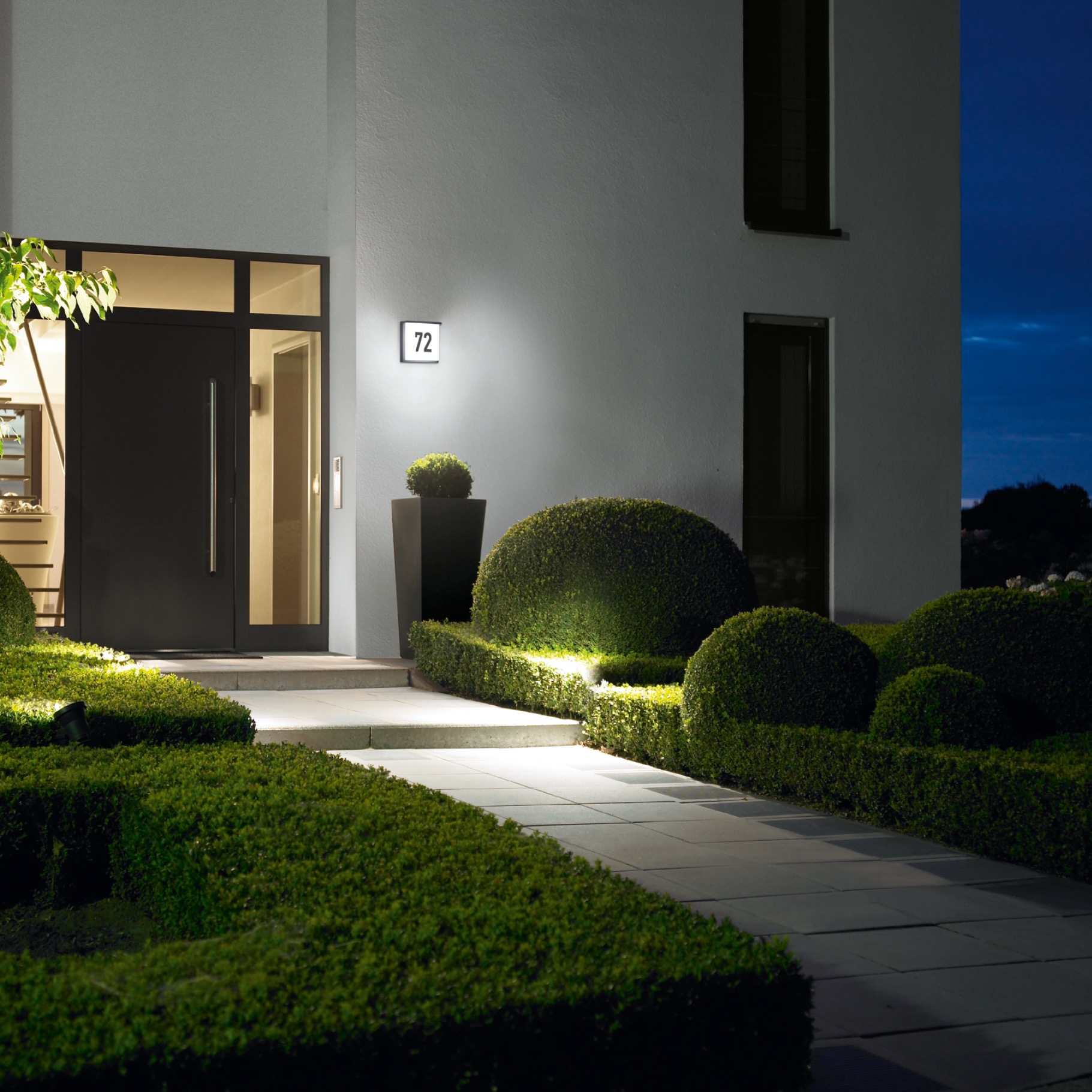 Moderner Hauseingang mit beleuchtetem Gartenweg, Hausnummernleuchte und LED-Außenbeleuchtung bei Nacht.