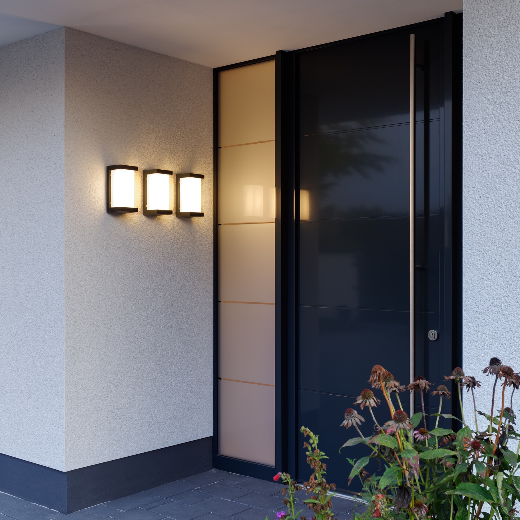 Drei LED-Wandleuchten neben einer modernen Haustür beleuchten den Eingangsbereich eines Wohnhauses.