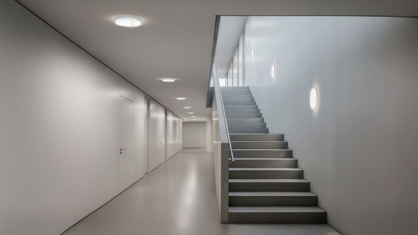 Scabra Decken- und Wandleuchten beleuchten ein modernes Treppenhaus mit gleichmäßigem, angenehmem Licht.