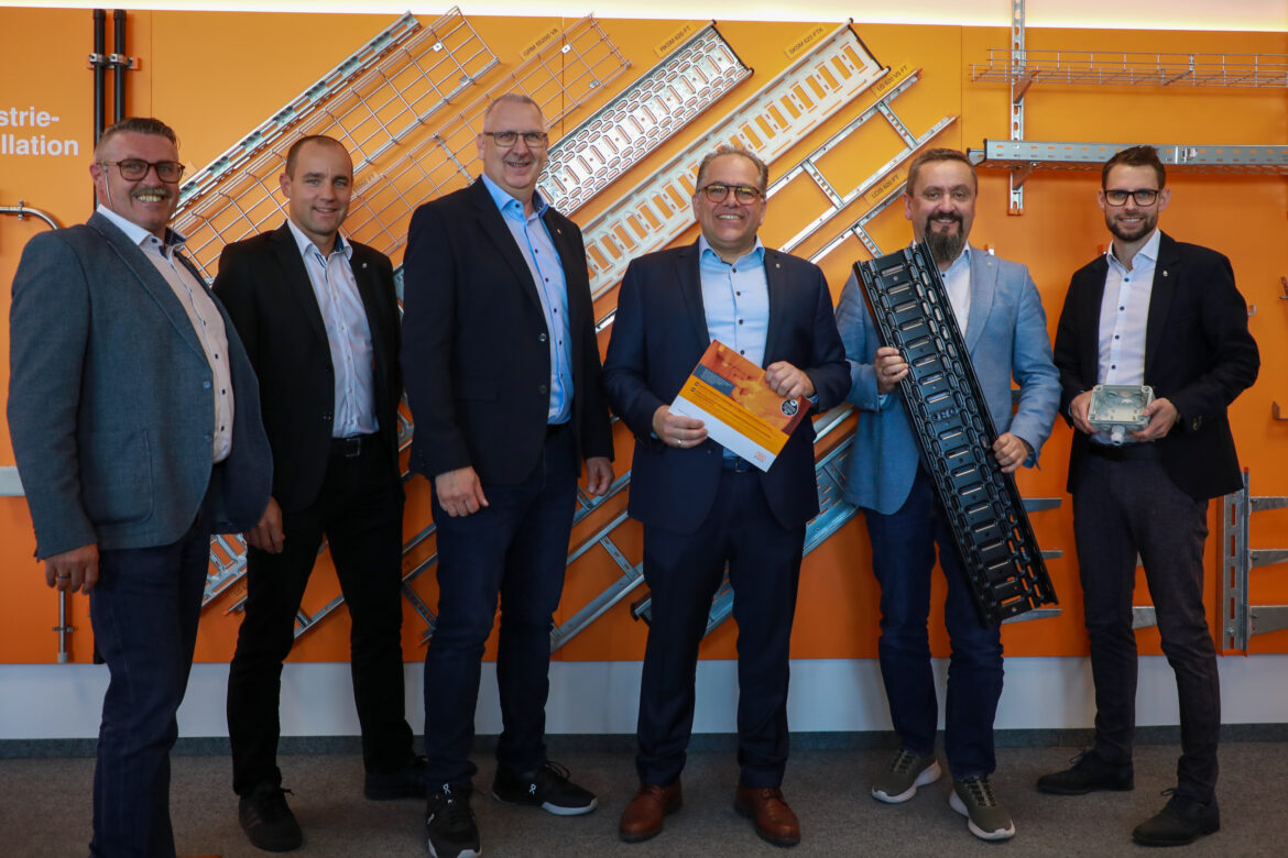 Team von Obo Bettermann Österreich vor Produktwand mit Kabeltragsystemen und Installationslösungen