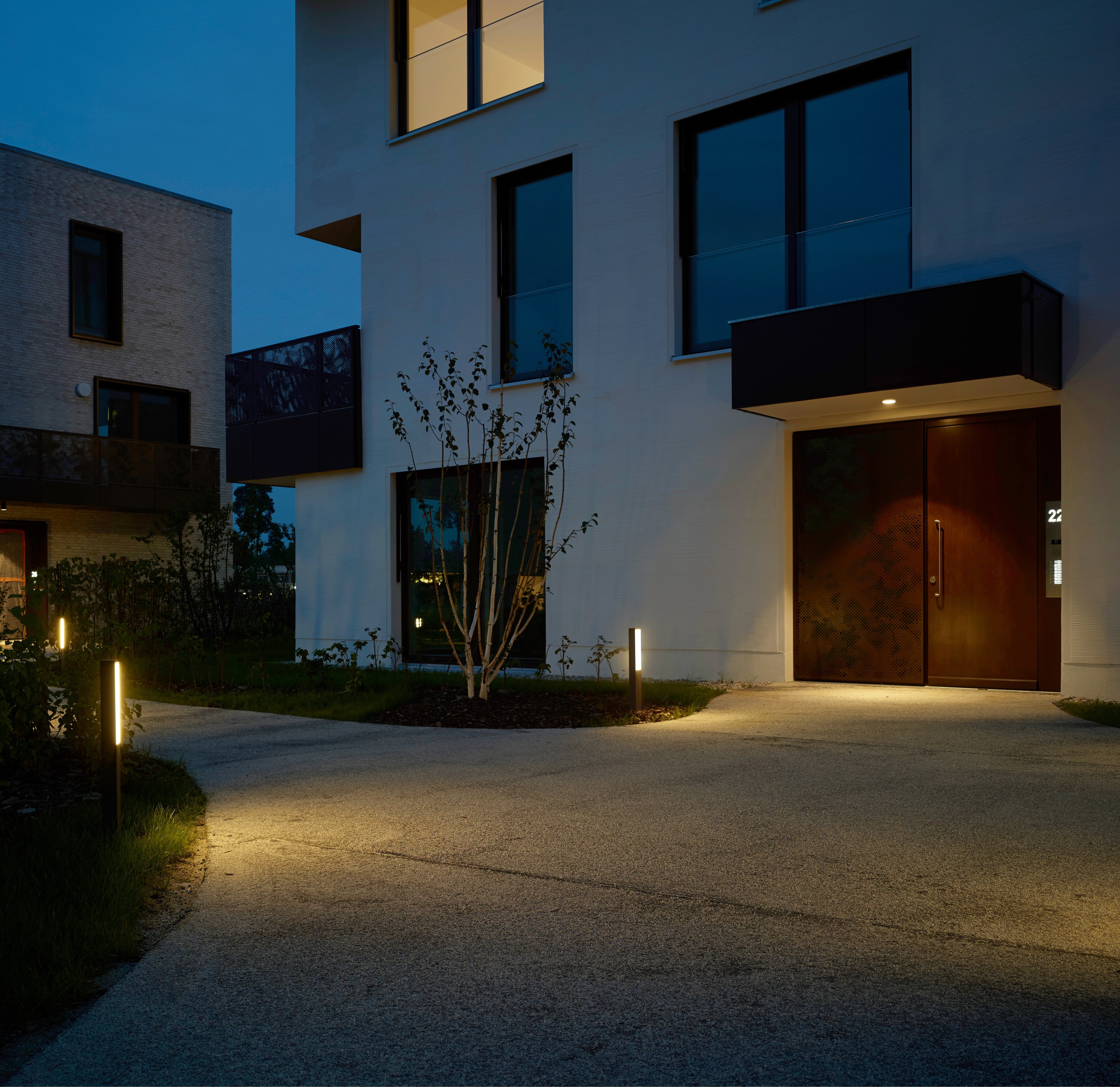 Modernes Wohnquartier bei Nacht mit LED-Pollerleuchten, beleuchtetem Hauseingang und Fassadenbeleuchtung.