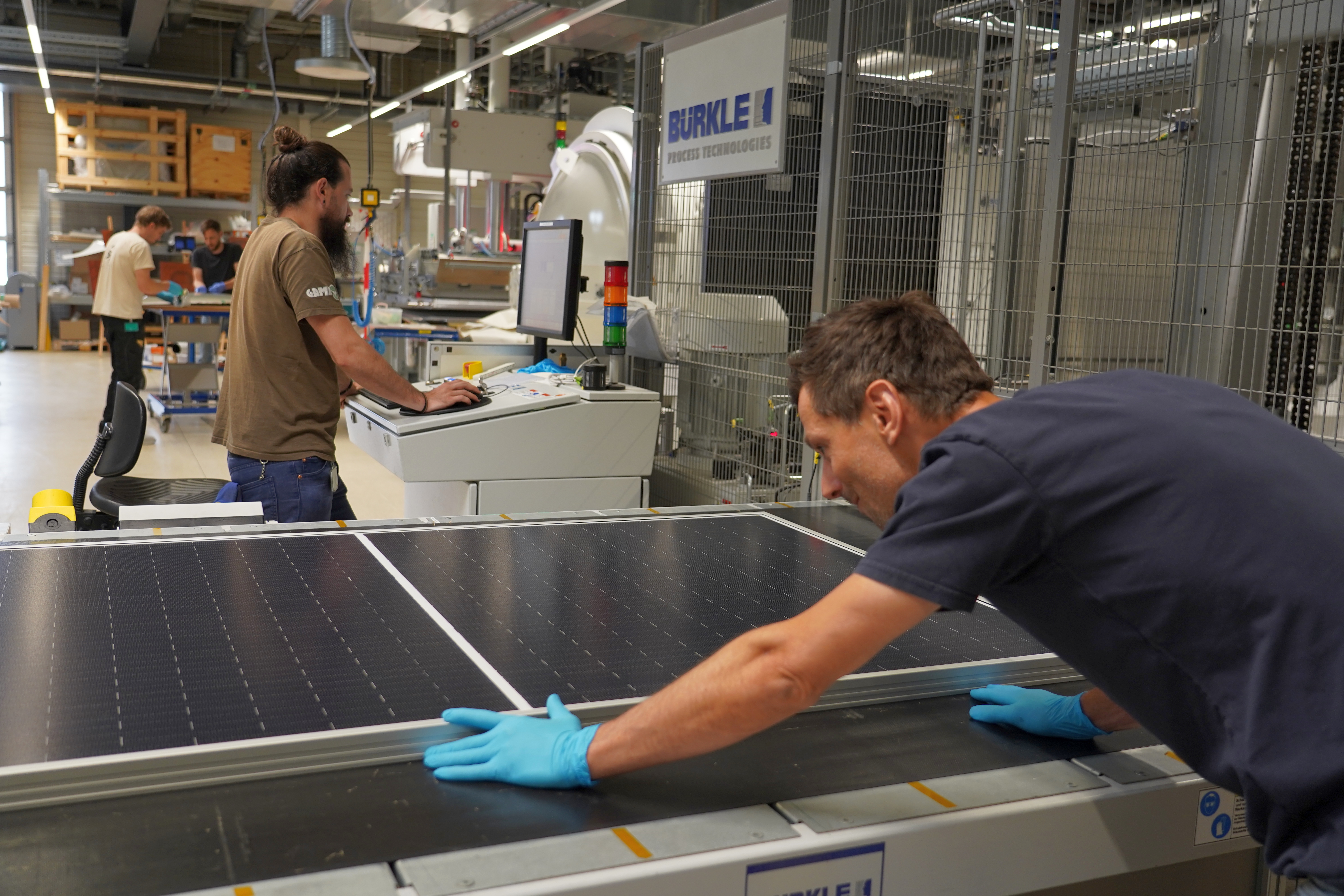 Mitarbeitende positionieren ein Perowskit-Silizium-Solarmodul an einer Produktionsanlage in einer Fertigungshalle.