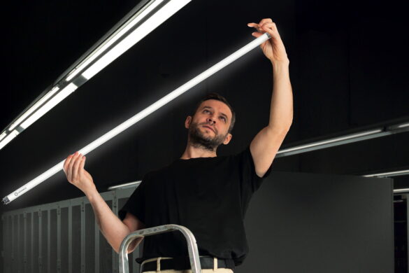 Techniker auf einer Leiter hält eine LED-Röhre bei Arbeiten an einer Beleuchtungsanlage.