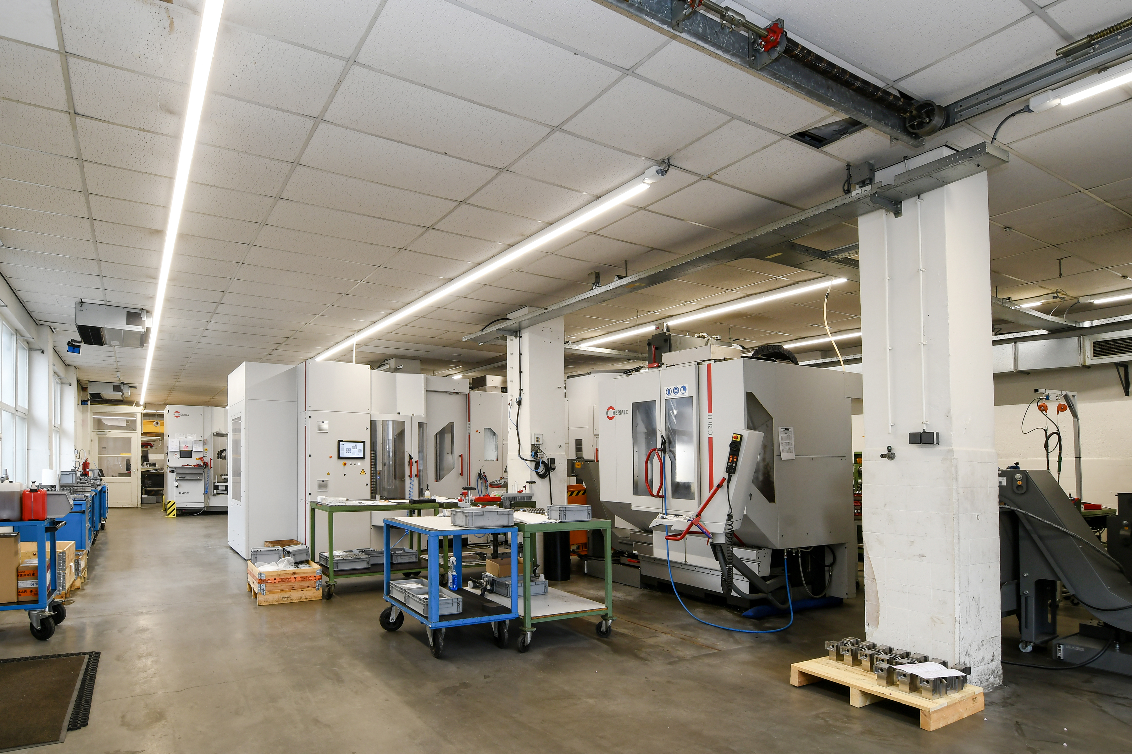Produktionshalle mit großen Maschinen und durchgehenden LED-Lichtlinien an der Decke.