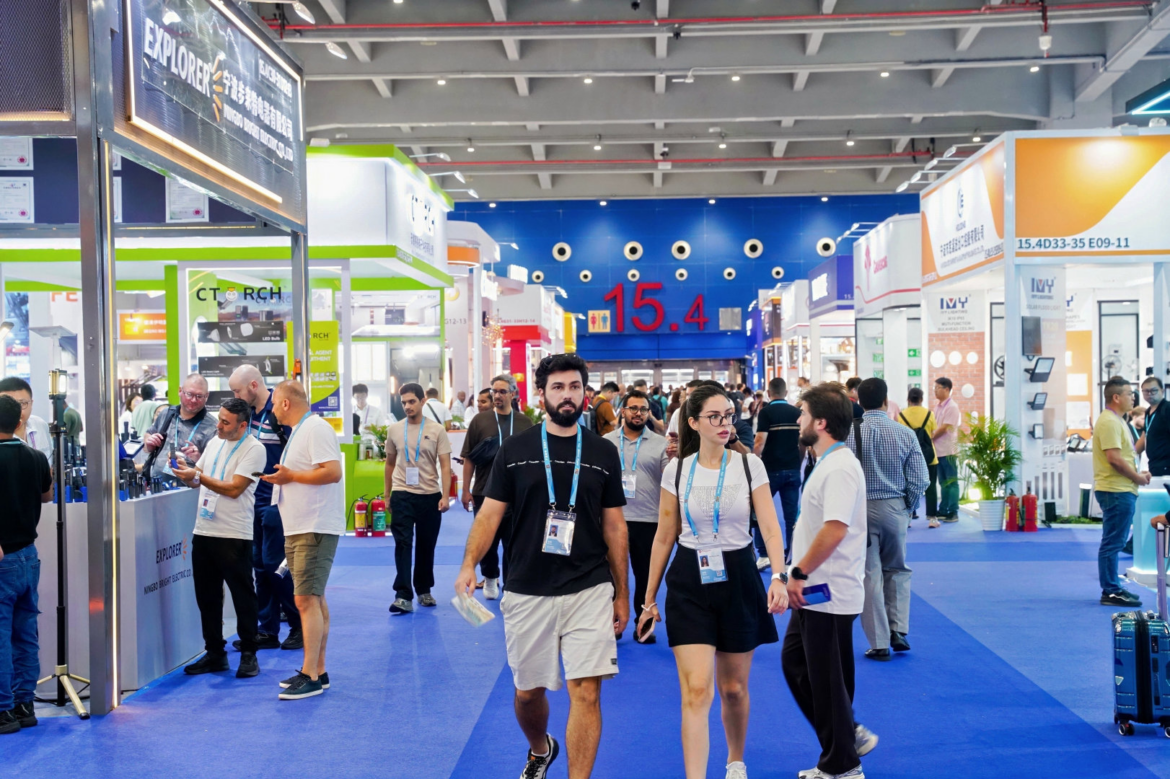 Internationale Fachbesucher gehen durch eine gut besuchte Messehalle der Canton Fair 2026, vorbei an Ausstellungsständen für Elektro- und Beleuchtungstechnik.